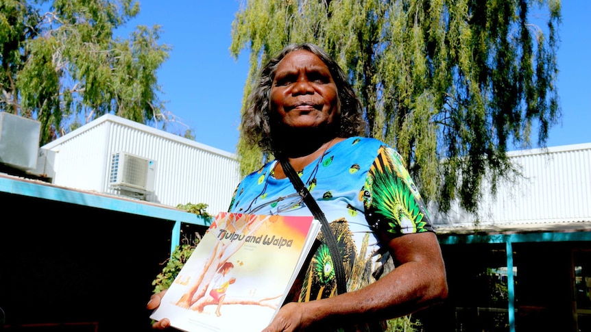 Alison 'Tjulapi' Carol holds a kids book called Tjulpu and Walpa