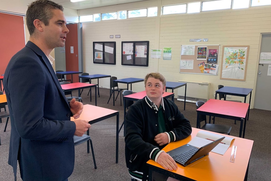 Ryan Hicklin sits at a desk and looks up at school principal Chris Quinn.