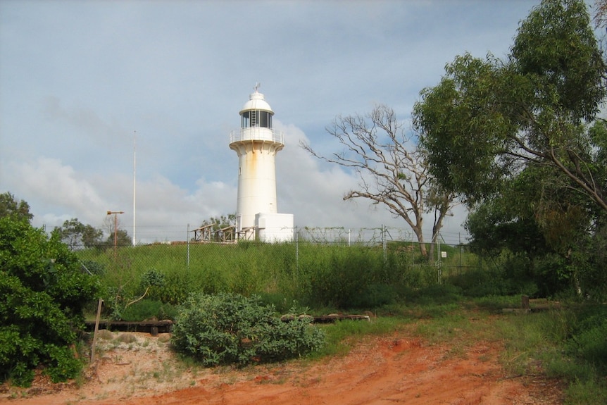 A white lighthouse surrounded by clouds and bush