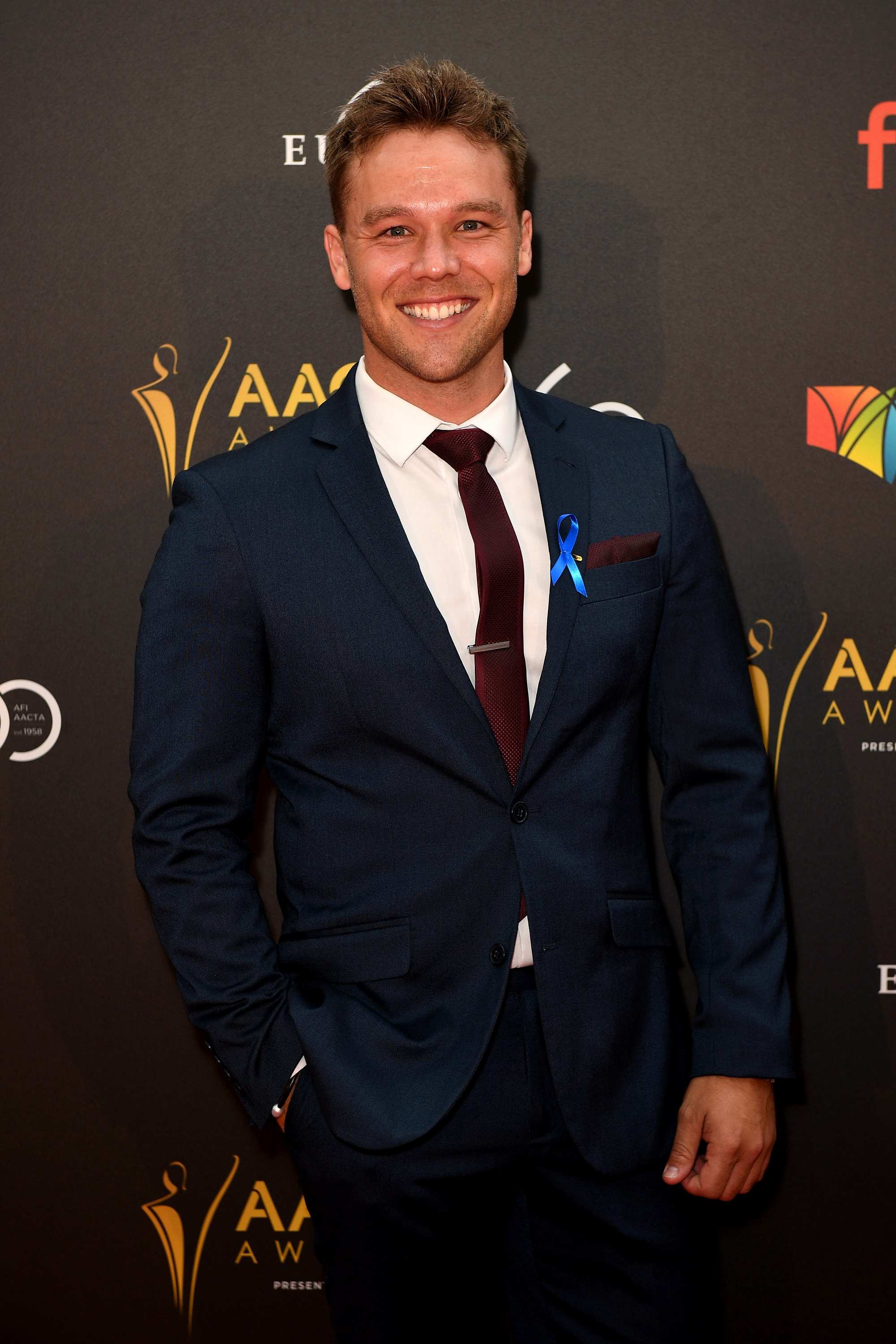 Lincoln Lewis poses on the red carpet in a suit jacket and tie.