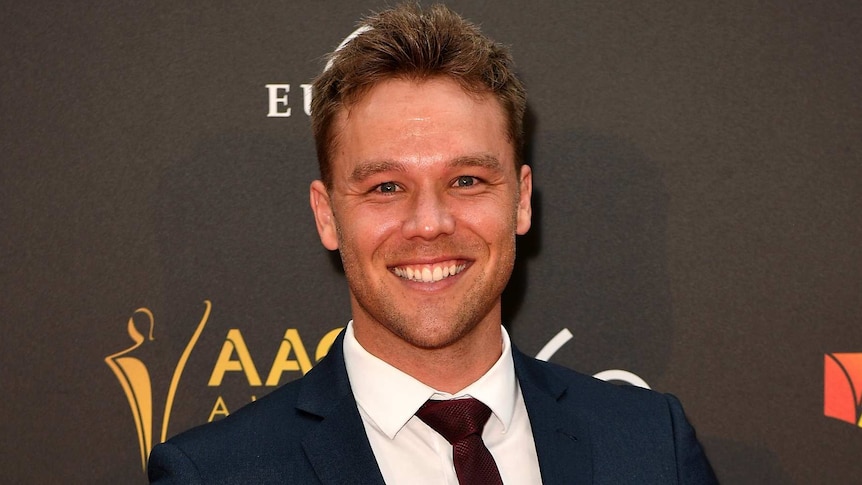 Lincoln Lewis poses on the red carpet in a suit jacket and tie.