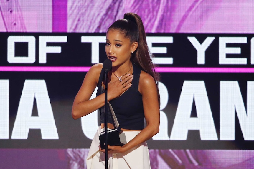 Pop star Ariana Grande accepts an award with her hand to her heart.