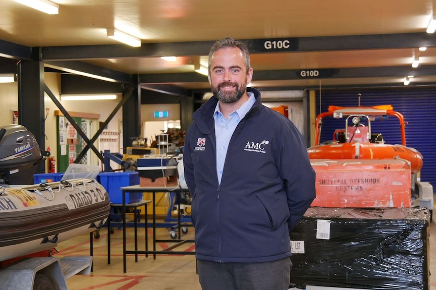 A man stands in front of maritime equipment smiling at the camera.