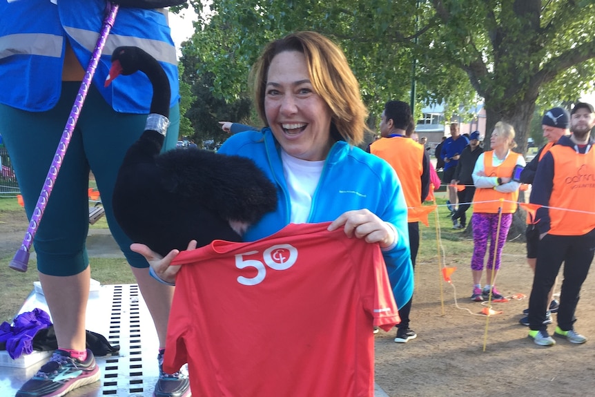 Lisa Millar holds up a red t-shirt with 50 on it.