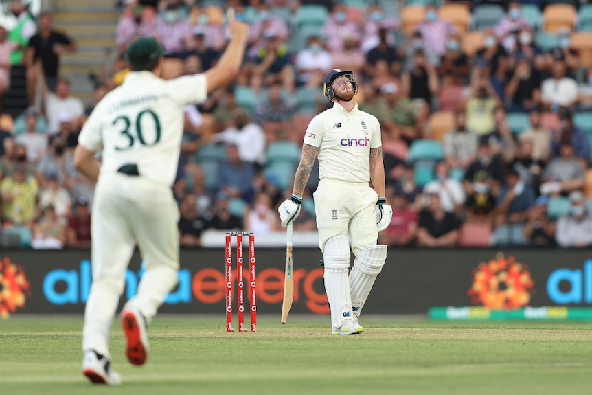 England batter Ben Stokes looks disappointed after getting out. Australia fielder Pat Cummins celebrates in the foreground.