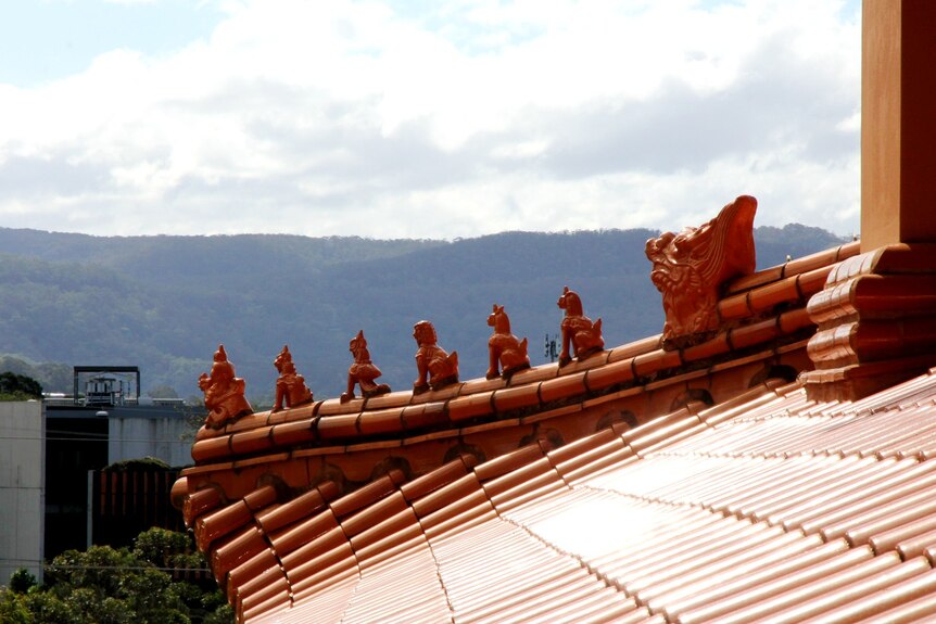 image of Buddhist temple roof in foreground with powerline, modern building and mountain in the background