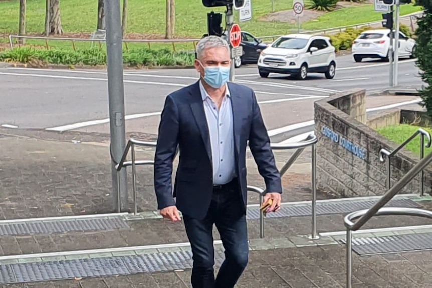 Ex-MP Craig Thomson, wearing a dark suit and mask, walks up the steps of Gosford court house.