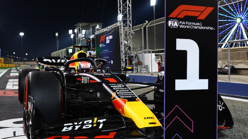A race car is parked off the track next to a big sign with the Formula 1 logo and a big '1' on it.  