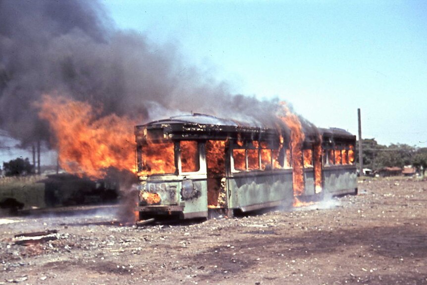 A tram burns in the middle of a scrap yard