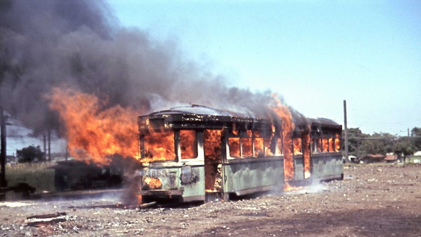 A tram burns in the middle of a scrap yard