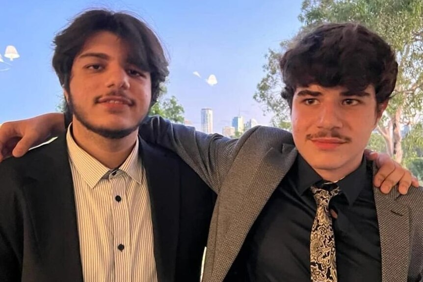 Two teenage brothers in suits with their arms around each other.