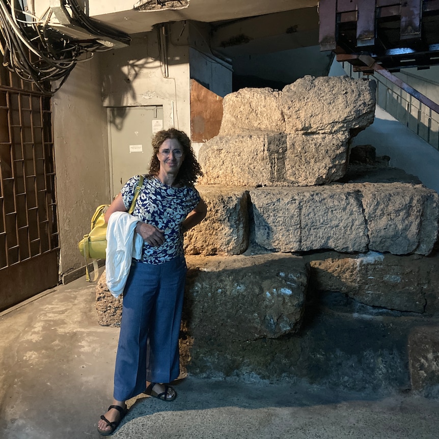 Annita Theocharaki standing in front of stone blocks of the ancient city walls of Athens, hidden in a basement 