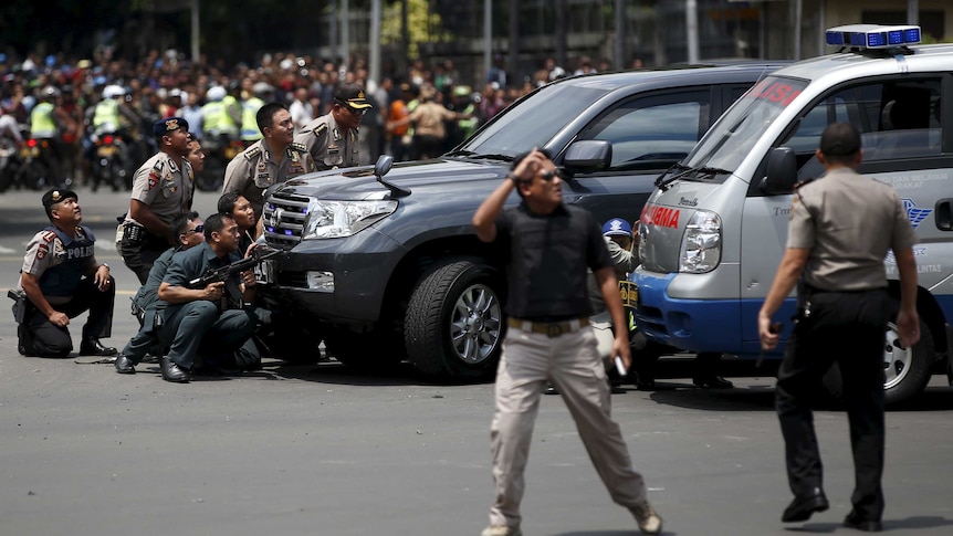 Police officers crouch behind vehicles, reacting to a series of explosions in the centre of Jakarta, Indonesia.