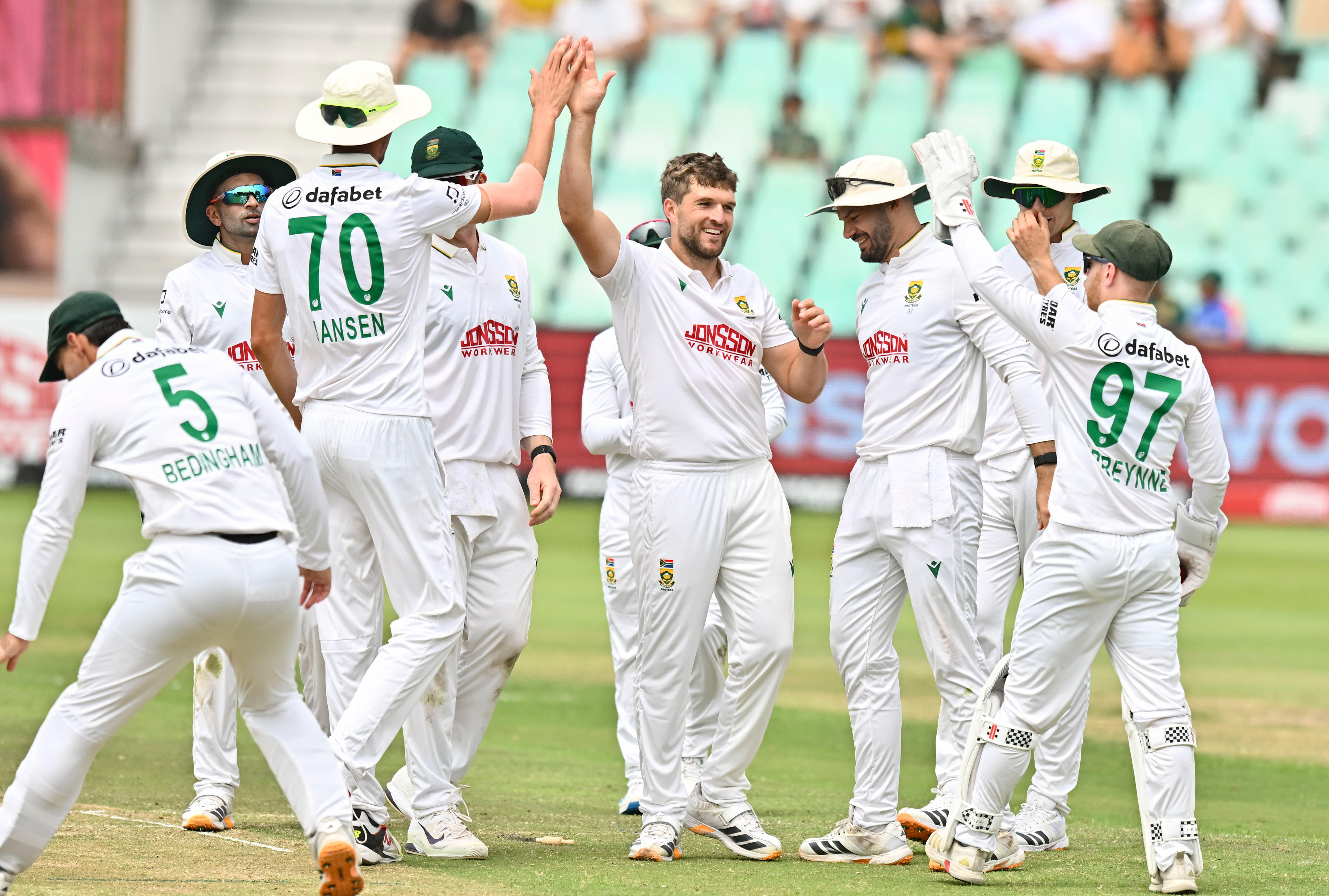 A South African bowler (centre) high-fives a teammate as other players surround him after a wicket.