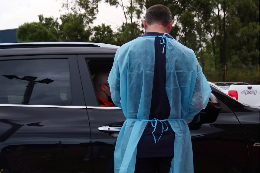 A medical worker wearing protective clothing stands at the car window of a person getting a covid test