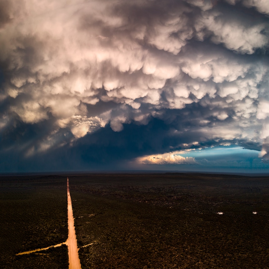 A dirt road is lit up by sun shining through storm clouds.