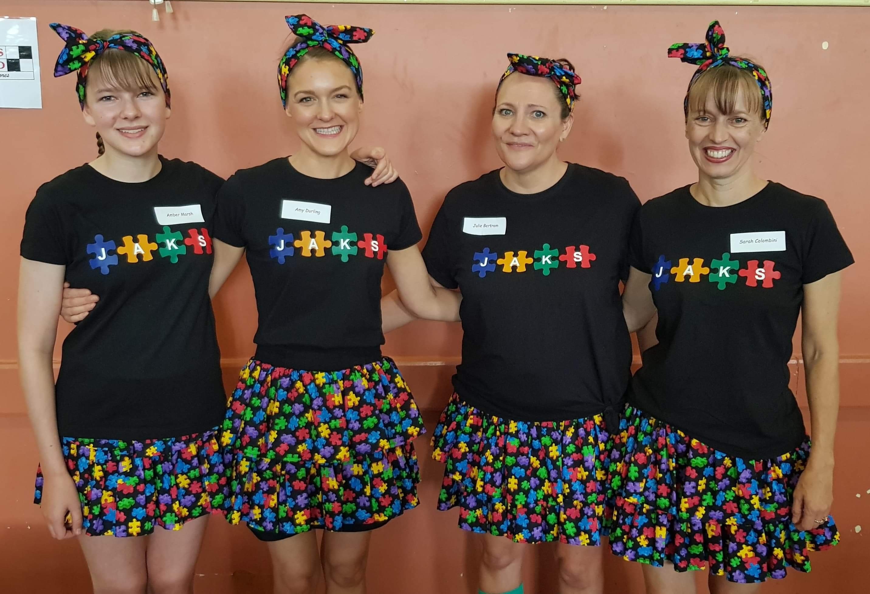 Four women wear clothing with colourful pieces of puzzles printed on their skirts and t-shirts