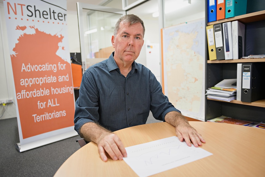 A man sits in an office looking sternly at the camera. 