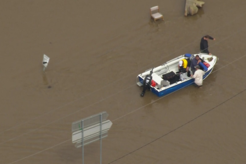 A tinnie floats past a highway sign through floodwaters.