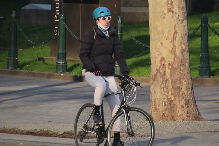 A woman wearing sunglasses sits on a stationary bicycle.