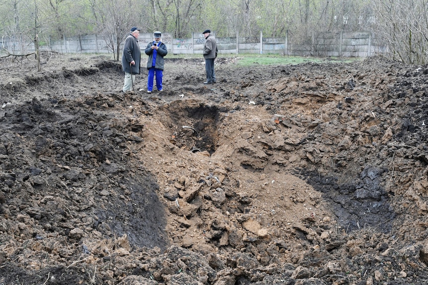 Men stand next to a huge crater after shelling