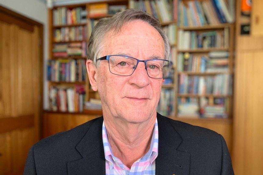 Professor Peter Collignon sits and looks into the camera with a bookcase behind him.