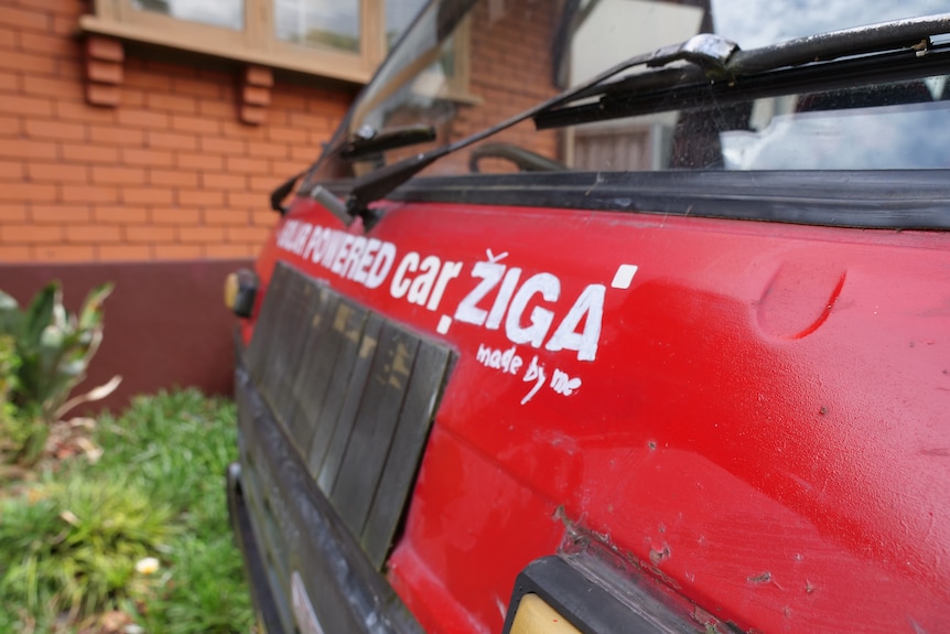 A written sign on the front of a red car that reads "solar powered car Ziga"