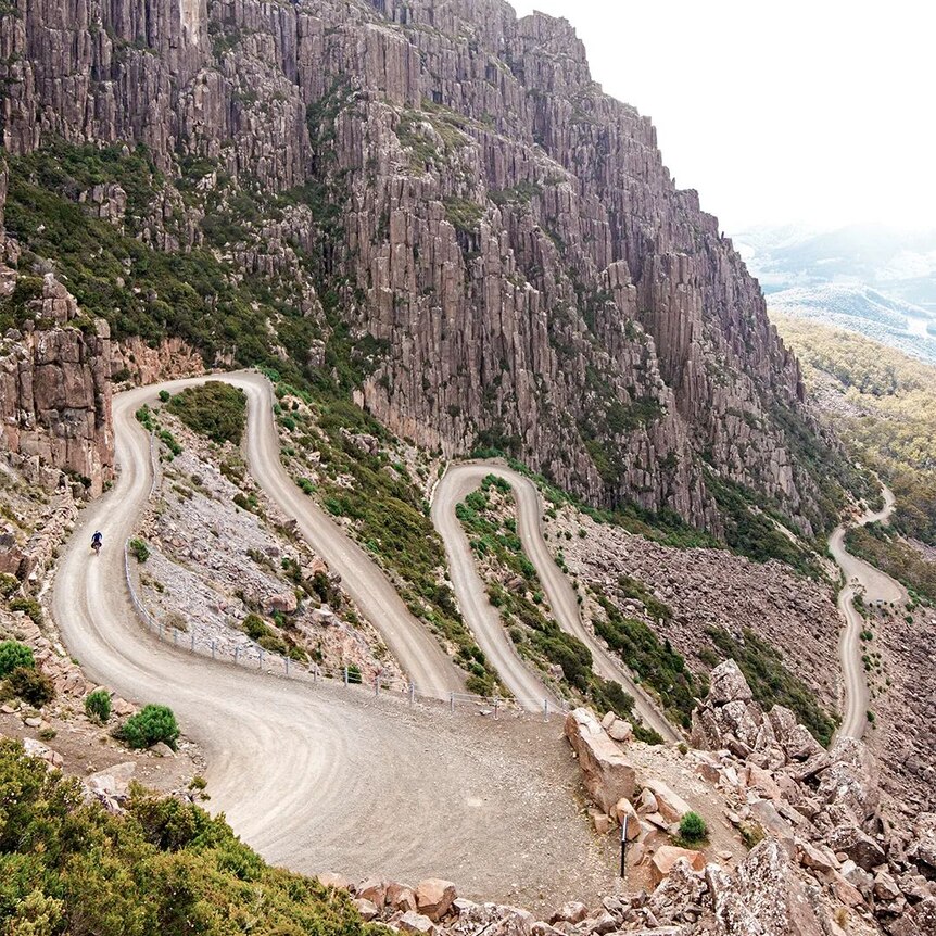 A cyclist at the top of a long windy road of switchbacks.