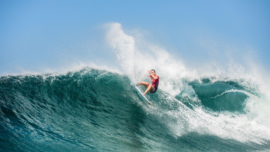 A woman rides a wave on her board.