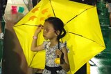 A girl carrying an umbrella walks past a replica of the Goddess of Democracy.