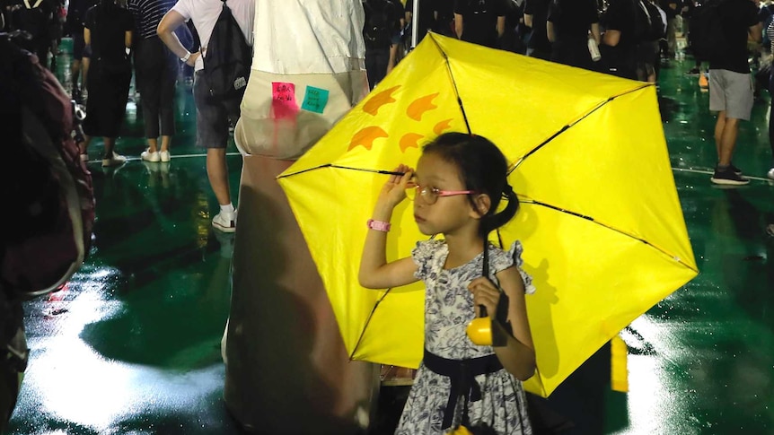 A girl carrying an umbrella walks past a replica of the Goddess of Democracy.