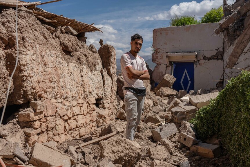 A man looks at the camera, while standing on a pile of rubble.