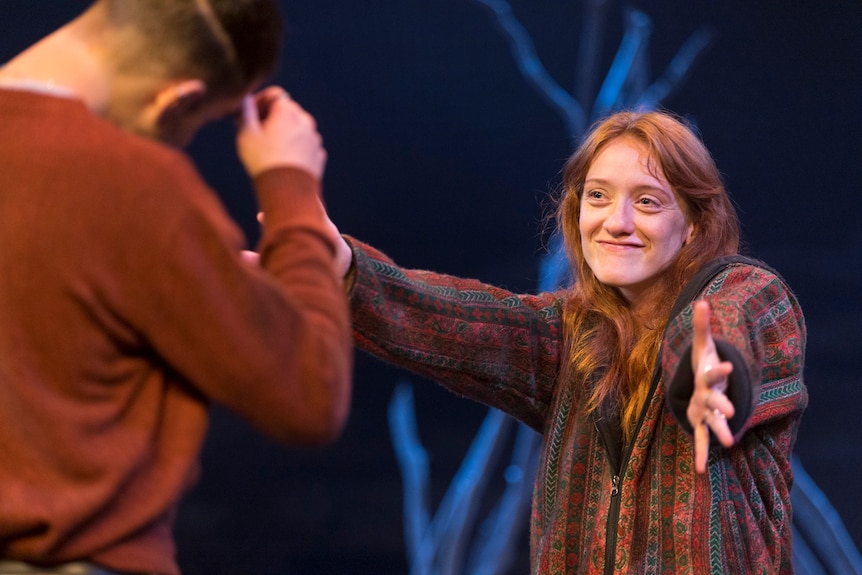 A woman with long red hair holds her arms out to embrace a man, smiling. The man's face is not seen.