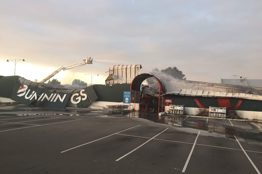 A Bunnings Warehouse store lies gutted with its roof collapsed after a major blaze, with firefighters in a crane hosing it down.