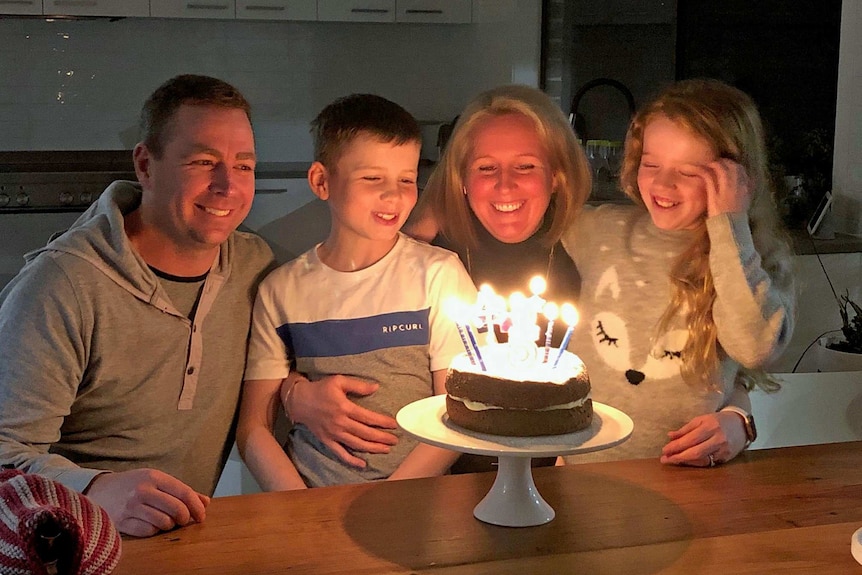 A man and woman and boy and girl look at a birthday cake.