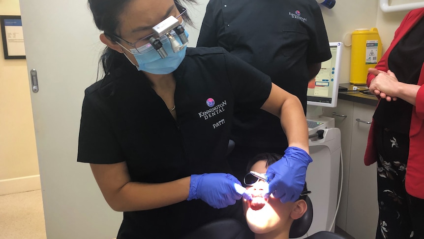 A boy sits in a dentist's chair as a dentist works on his mouth.