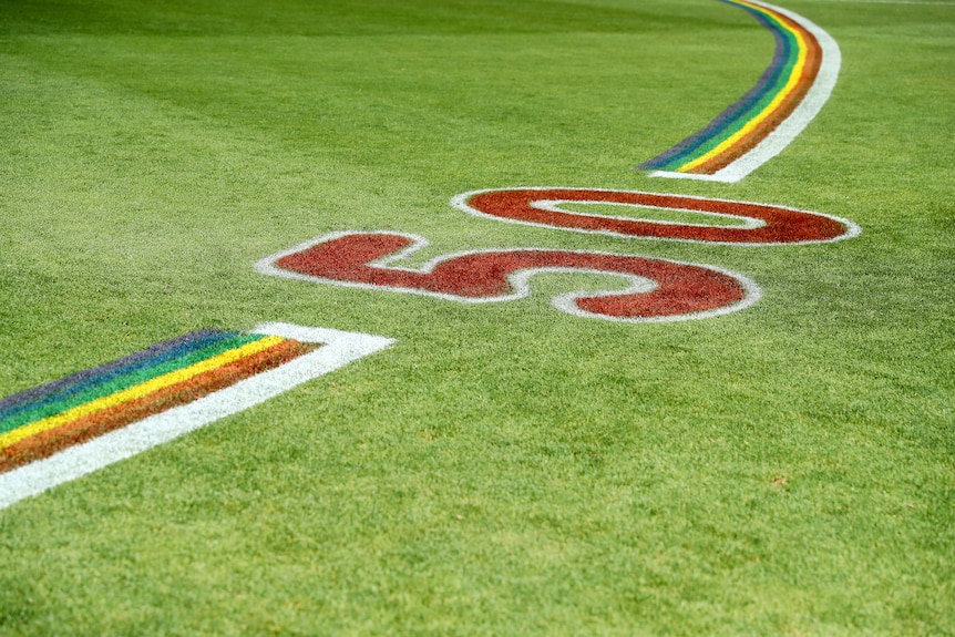 A rainbow arc on a grass AFL field with a big "50" painted in the middle.