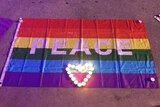 A rainbow flag with the word peace written in capitals and a love heart shaped from candles on the ground.