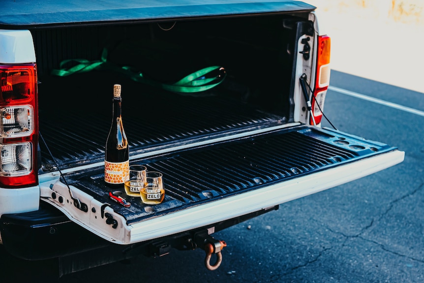 A wine bottle with a cork and glasses on the back of a white ute