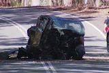 A completely smashed and burnt small car on a country road