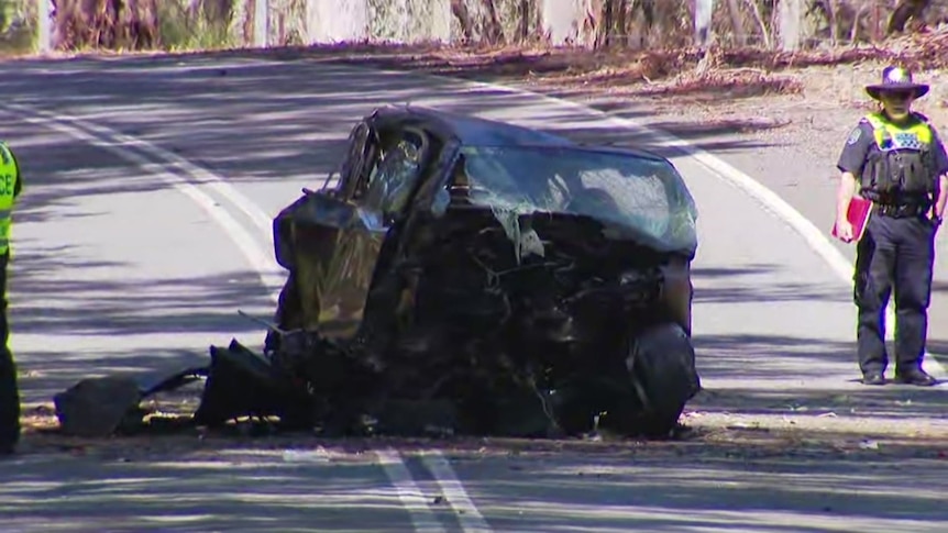 A completely smashed and burnt small car on a country road