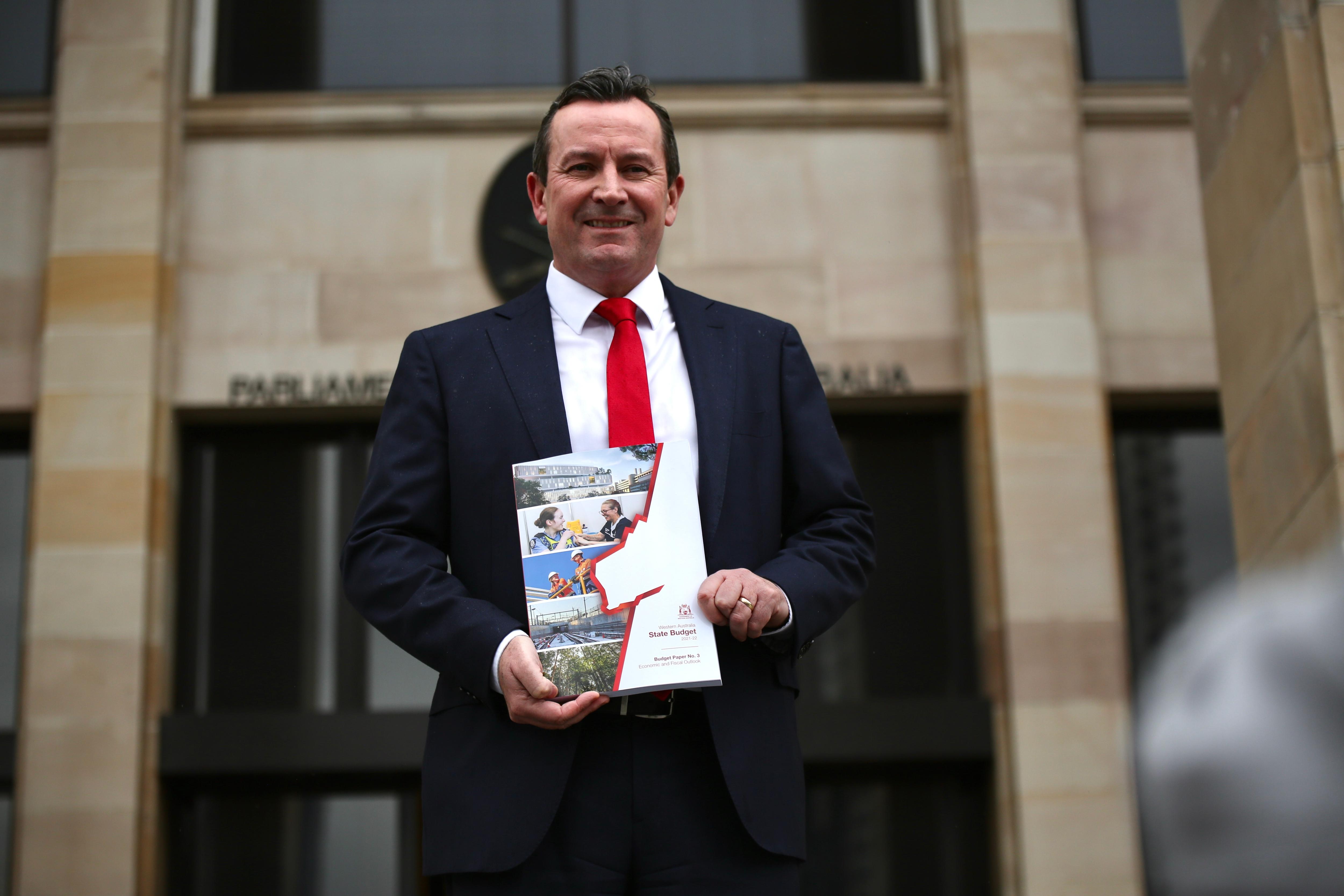 A man wearing a red tie holding a booklet on the steps of WA's parliament.