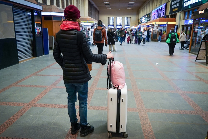 Женщина в красном шарфе и шапочке держит чемодан на вокзале Хельсинки.