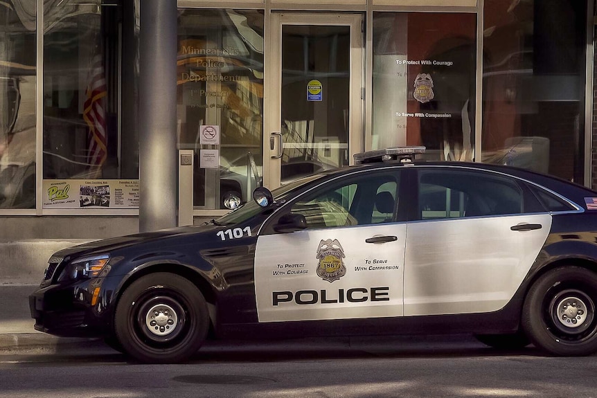 An American police car sits out front of Minneapolis police glass shopfront