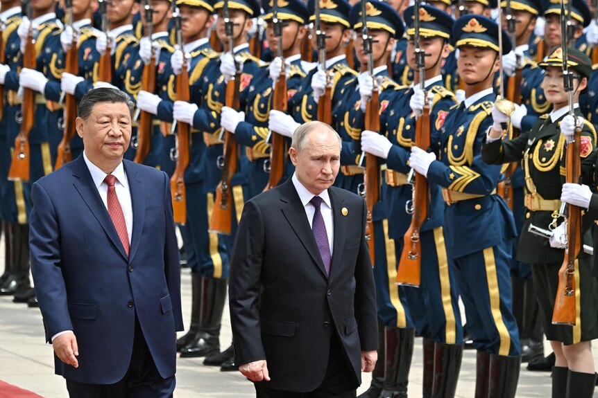 The leaders of China and Russia are walking past a presidential welcoming ceremony wearing suits.