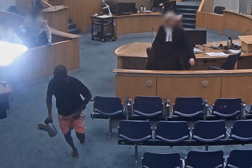 A CCTV screenshot of a man running through a courtroom holding a silver jug. 