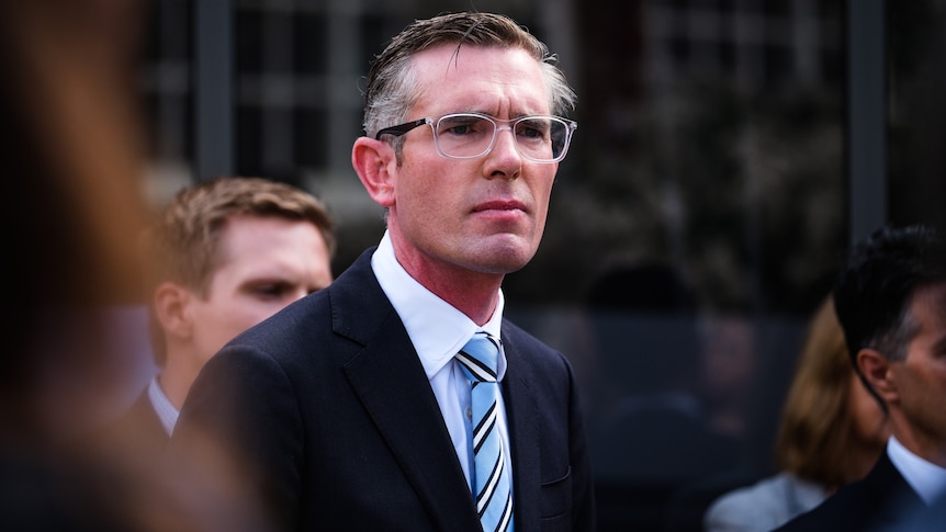 a man wearing glasses standing outdoors in front of a media pack 