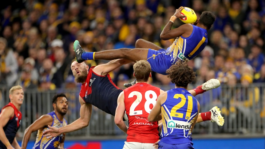 Liam Ryan catches a yellow ball lying horizontally at head height in front of two watching players