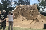 Two people look at a sand sculpture.