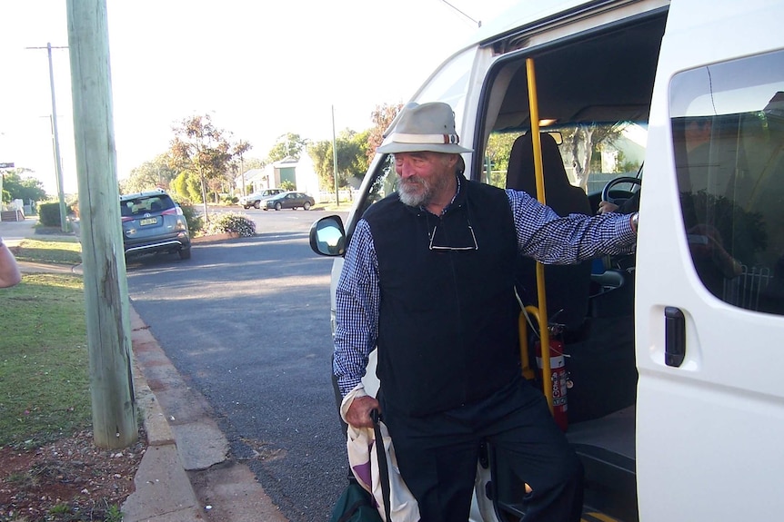 A man holding an overnight type bag stepping onto a mini bus